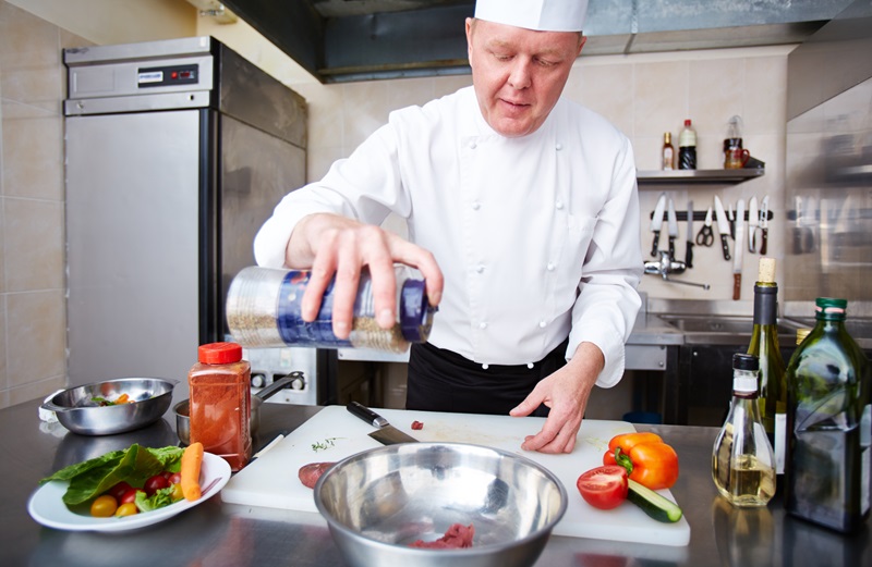 Image of male chef adding spices to meat in bowl