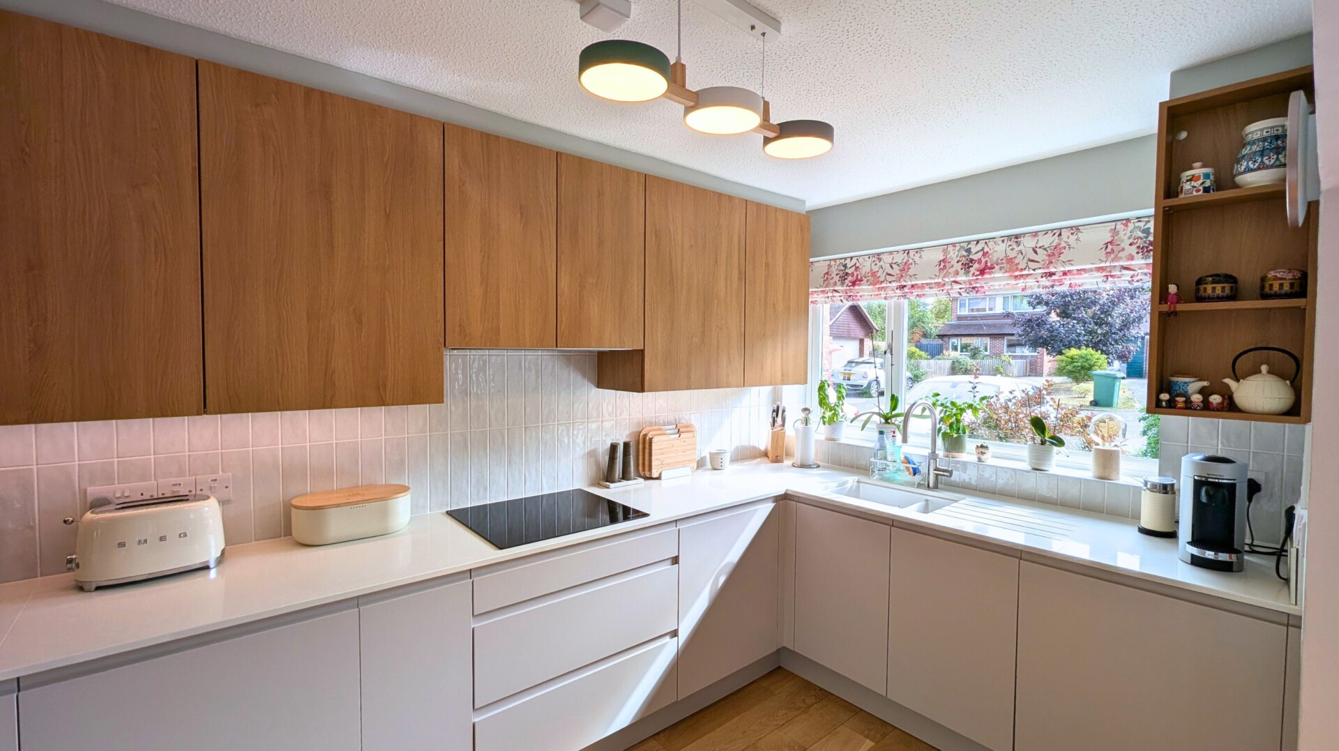 A modern, handleless kitchen with light grey and warm wood cupboards, and modern pendant lighting.