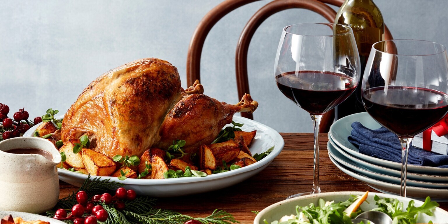 A roast turkey and glass of wine sit on a festively decorated dining table